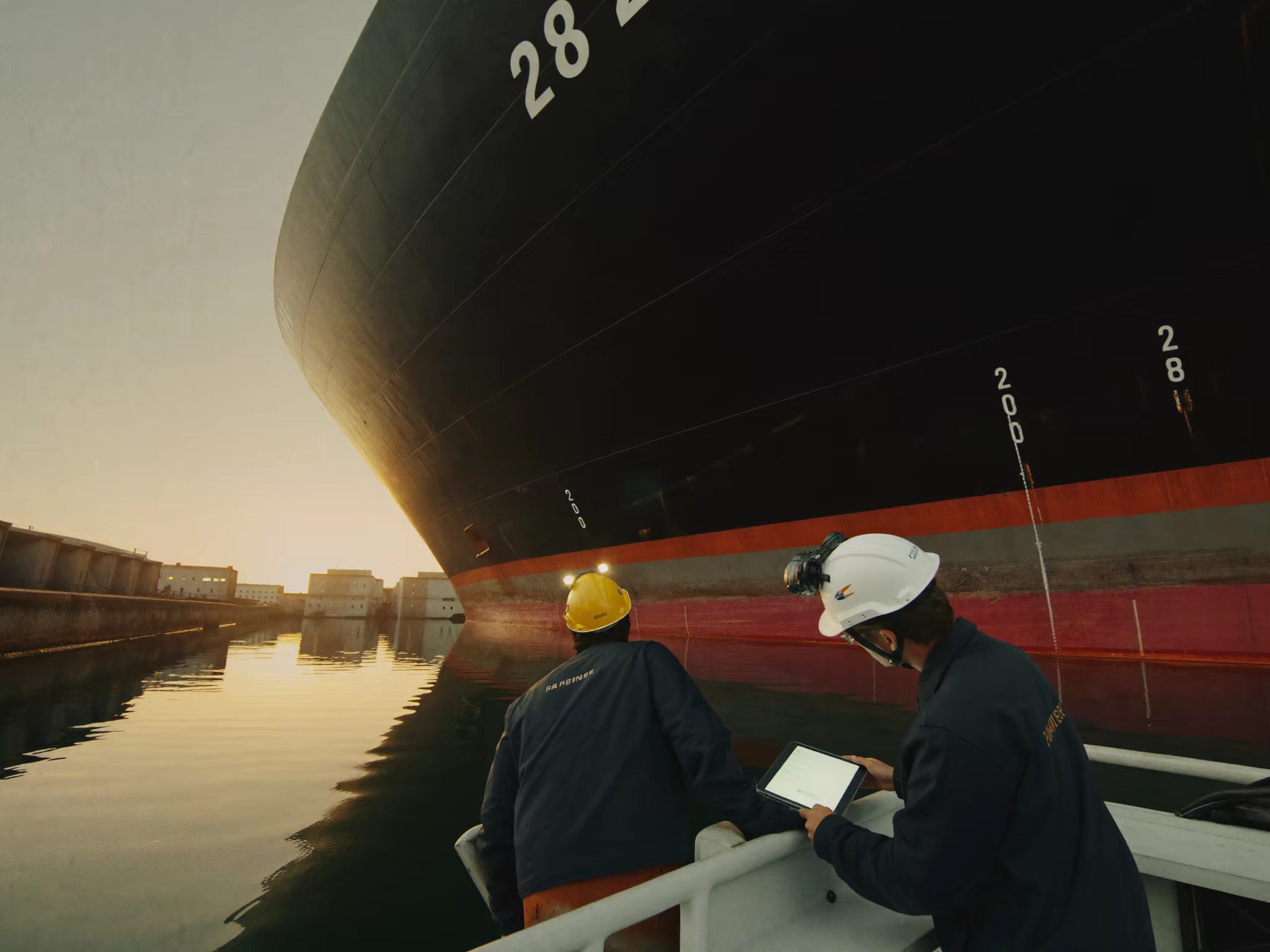 Workers in a small boat inspecting the hull of a large cargo ship